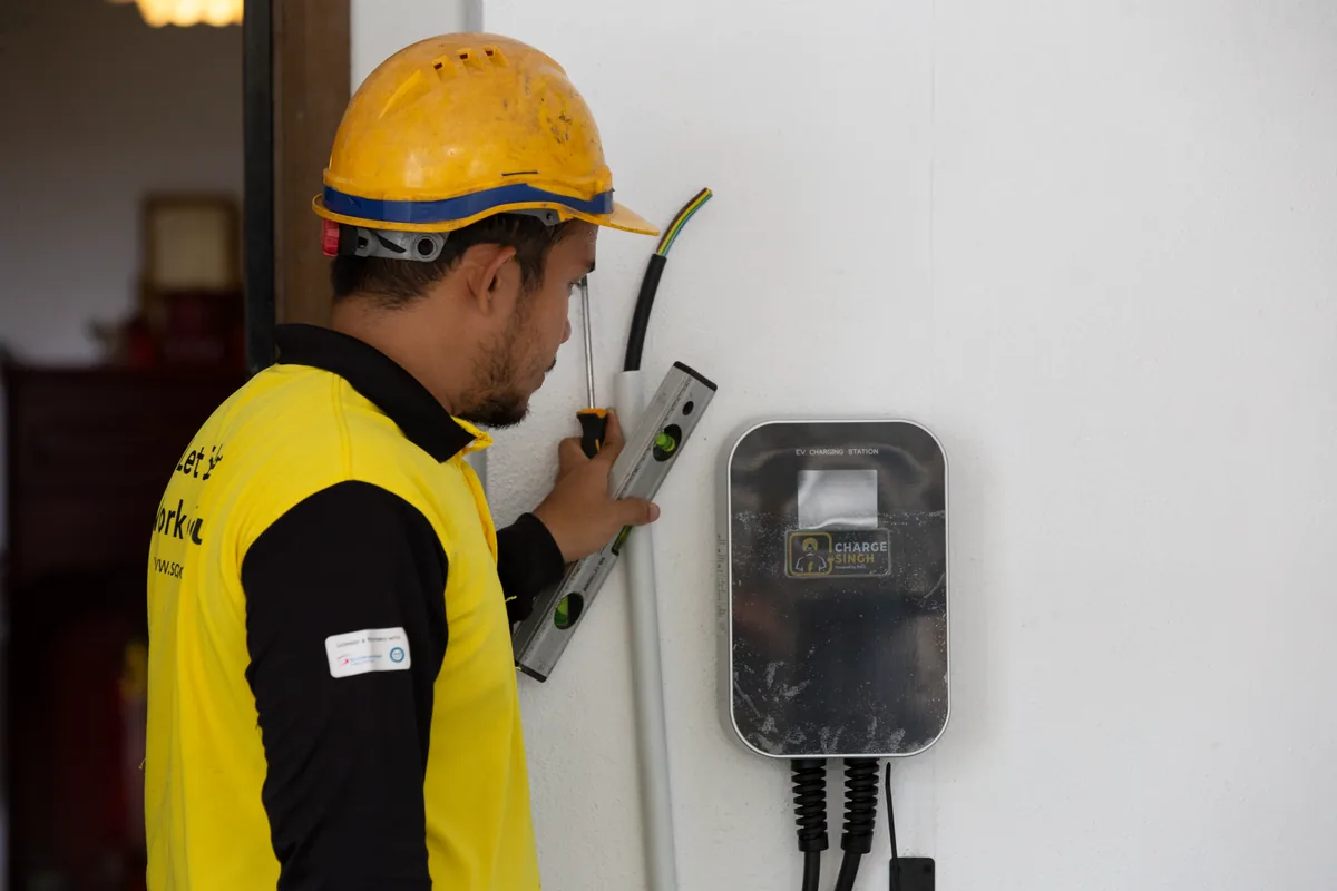 An installer in a hard hat wiring a ChargeSingh charger on a white wall