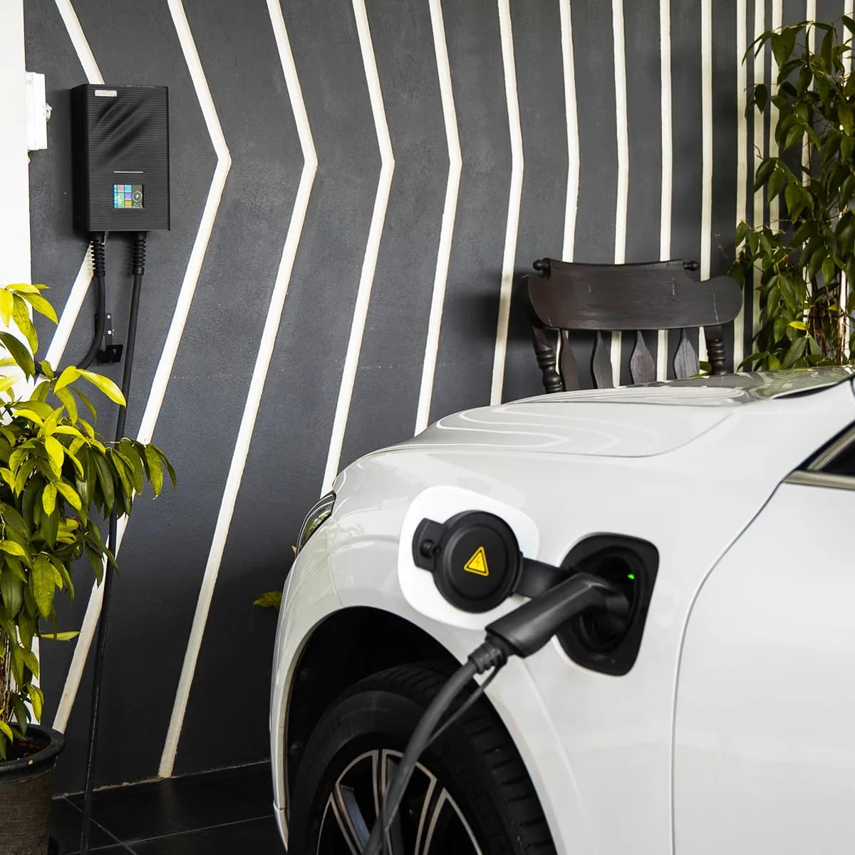 An RDX-3 charger on a porch wall, its cable plugged into a white car parked beside it